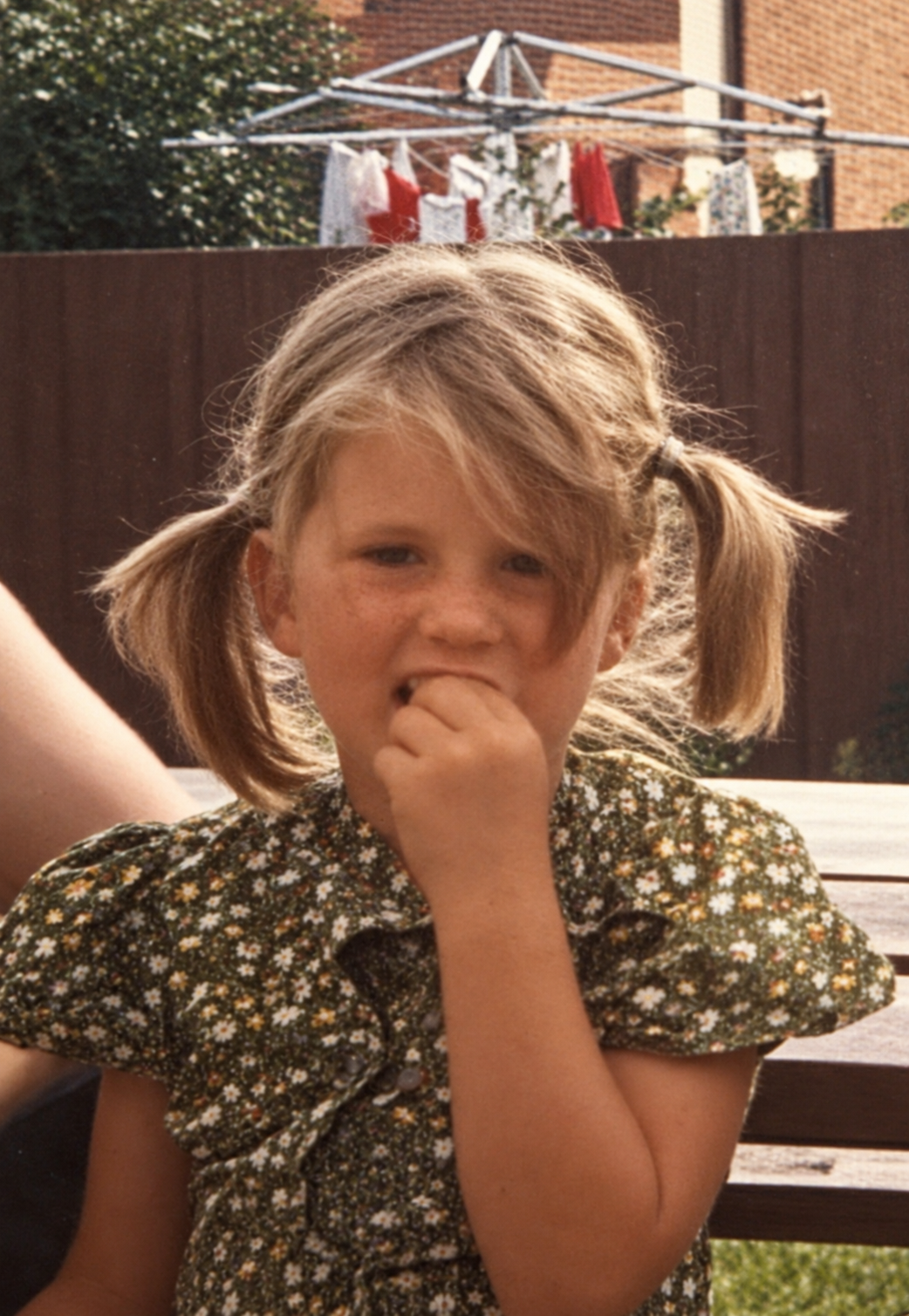 Childhood photograph of the artist wearing an olive-green floral shirt in a sunny backyard.