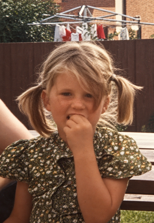 Childhood photograph of the artist wearing an olive-green floral shirt in a sunny backyard.