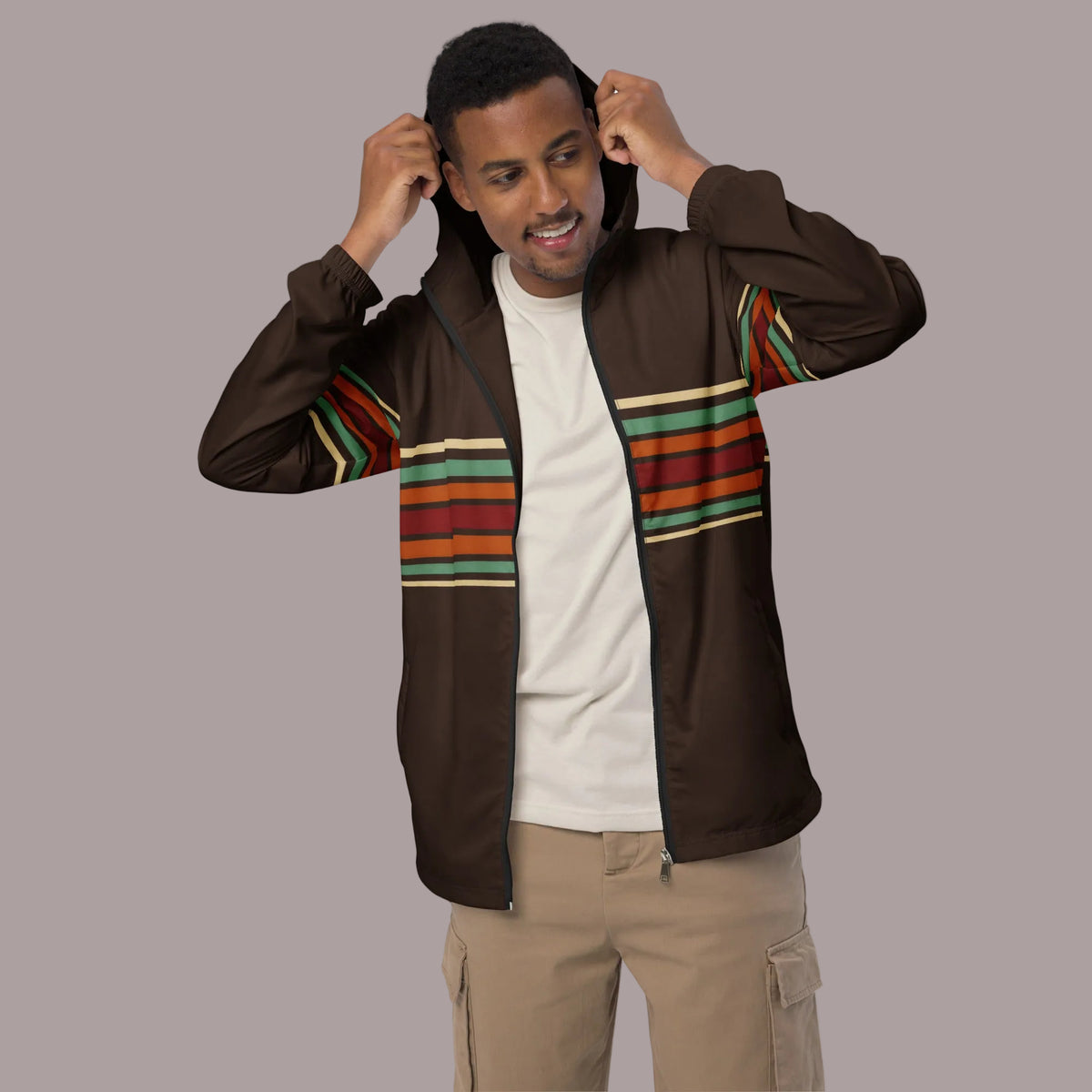 A man wearing a brown zip-up hoodie with colorful striped panels on the chest and sleeves, styled over a white t-shirt and beige cargo pants, set against a plain white background.