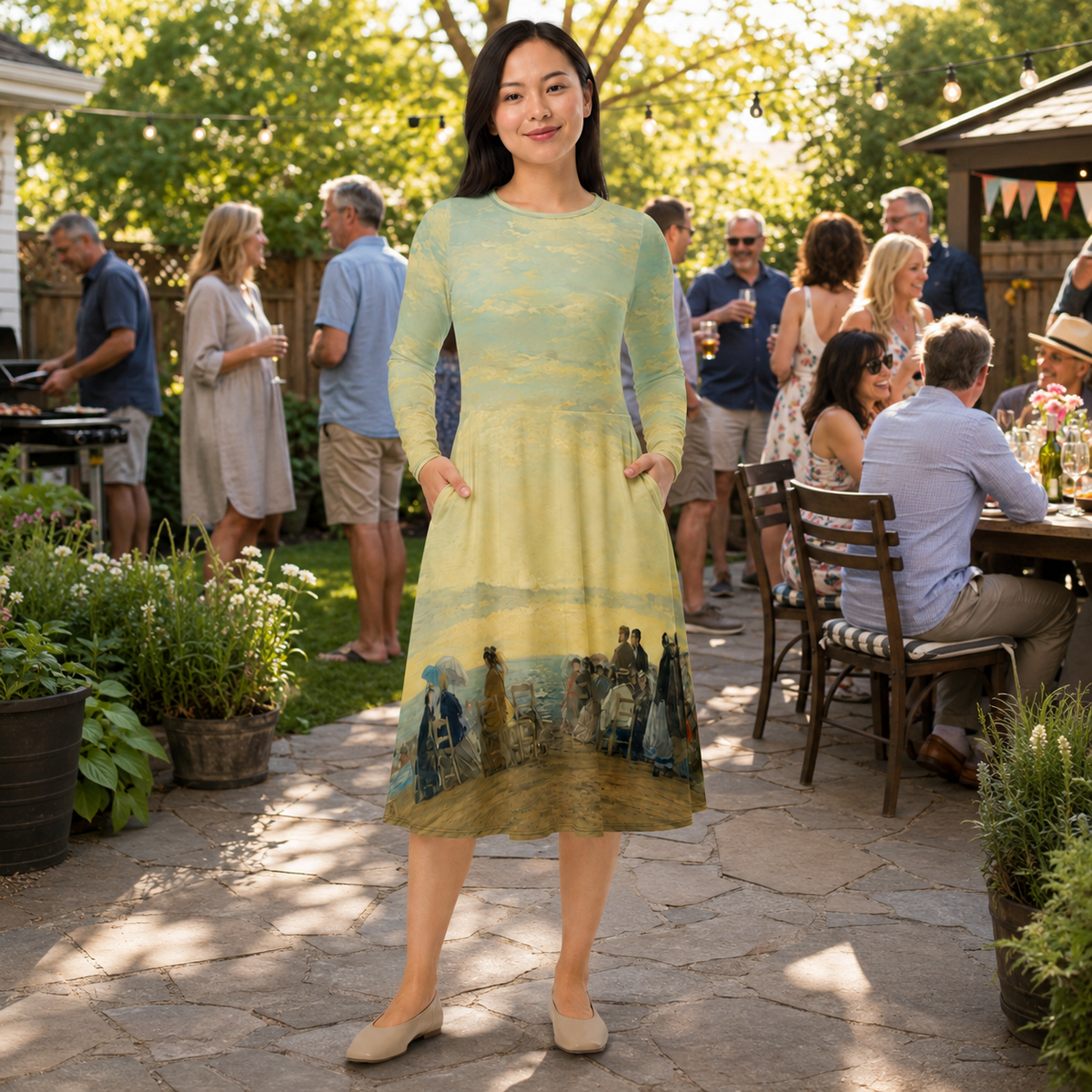 A woman stands outdoors in a backyard patio setting wearing a long-sleeve midi dress with a pale yellow and green landscape print and a dark blue scenic lower section. Guests are visible dining and socializing in the background.